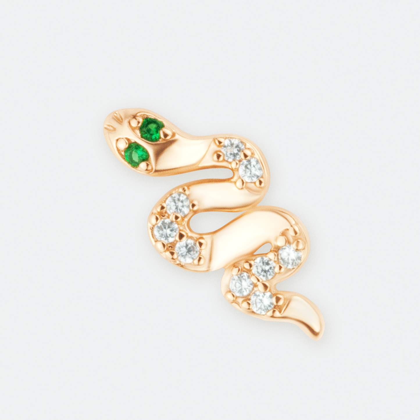 The Venefica earrings by Ocarina, 18K gold-plated snake-shaped stud earrings adorned with shimmering zircon stones and striking green gemstone eyes. A bold and mystical jewelry piece symbolizing transformation and power, displayed against a clean white background.